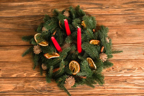 Vue de dessus de la couronne de Noël avec des bougies rouges et des branches vertes sur la surface en bois — Photo de stock