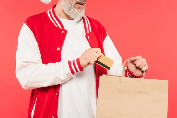 Visão cortada de homem de meia idade colocando cartão de crédito em saco de compras isolado no vermelho — Fotografia de Stock