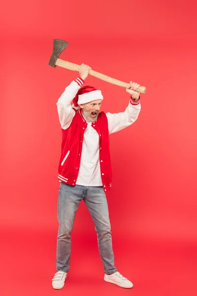 Volle Länge des Mannes mittleren Alters mit Weihnachtsmann, der die Axt über dem Kopf hält und auf Rot schreit — Stockfoto