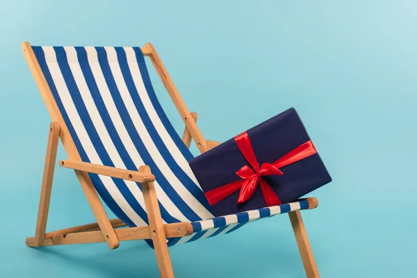 Present on striped deck chair on blue background — Stock Photo