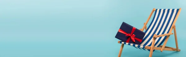 Present on striped deck chair on blue background, banner — Stock Photo