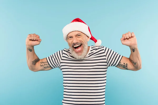 Excited middle aged man in stiped t-shirt and santa hat isolated on blue — Stock Photo