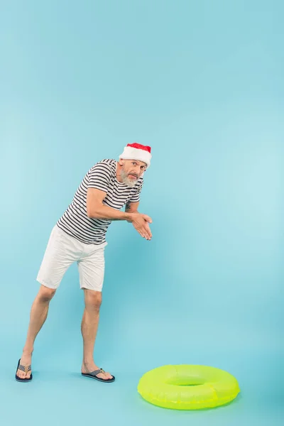 Full length of middle aged man in stiped t-shirt and santa hat imitating diving near swim ring on blue — Stock Photo