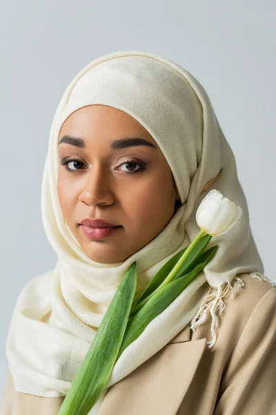 Giovane donna musulmana in hijab con tulipano isolato su grigio — Foto stock