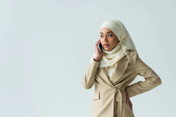 Stylish muslim woman in hijab and beige suit talking on smartphone isolated on grey — Stock Photo