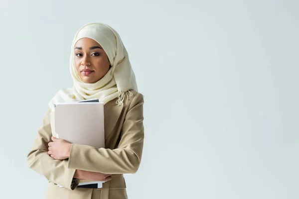 Стильна мусульманська бізнес-леді в хіджабі і бежевому костюмі, що тримає папки ізольовані на сірому — стокове фото