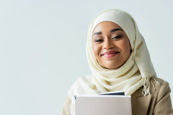 Muslimische und glückliche Geschäftsfrau im Hidschab hält Ordner isoliert auf grau — Stockfoto