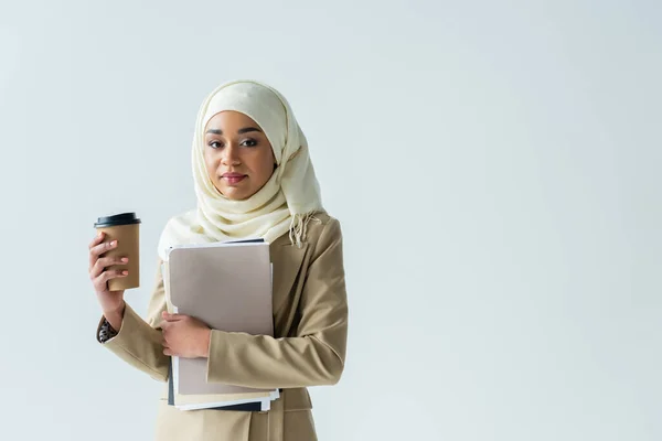 Femme d'affaires musulmane dans le hijab tenant des dossiers et une tasse en papier isolé sur gris — Photo de stock