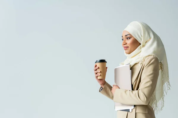 Mulher de negócios muçulmana em hijab segurando pastas e copo de papel isolado em cinza — Fotografia de Stock