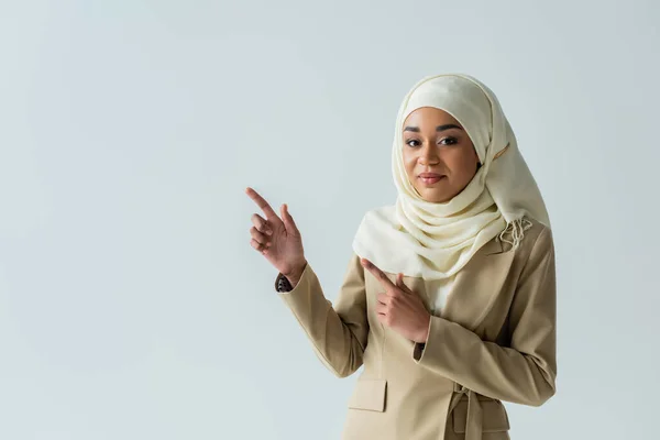 Muslim woman in hijab and beige suit pointing with fingers isolated on grey — Stock Photo