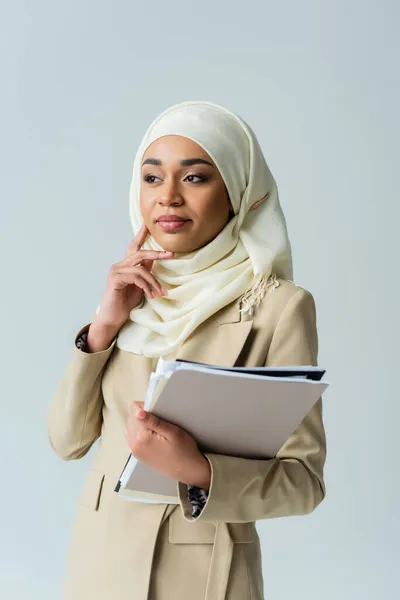 Donna d'affari musulmana in hijab in possesso di cartelle e pensare isolato su grigio — Foto stock