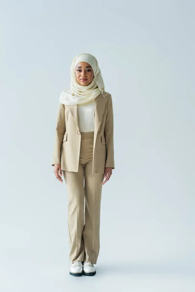 Full length of muslim woman in hijab and beige suit standing on grey — Stock Photo