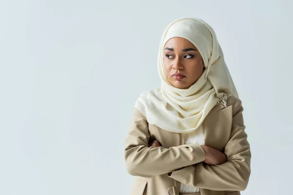 Ofendida mujer musulmana en hiyab de pie con los brazos cruzados aislados en gris - foto de stock