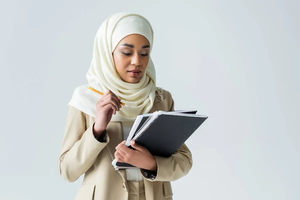 Mulher muçulmana em hijab segurando lápis e pastas isoladas em cinza — Fotografia de Stock