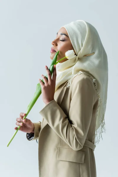 Мусульманська жінка з закритими очима тримає тюльпан ізольовано на сірому — стокове фото