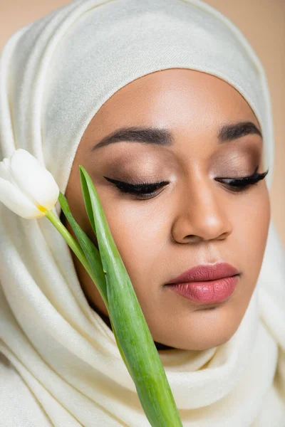 Portrait of young muslim woman in hijab near tulip isolated on beige — Stock Photo