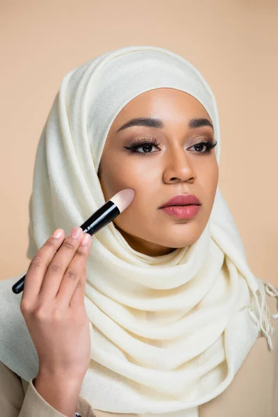 Jeune femme musulmane en hijab appliquant fond de teint isolé sur beige — Photo de stock