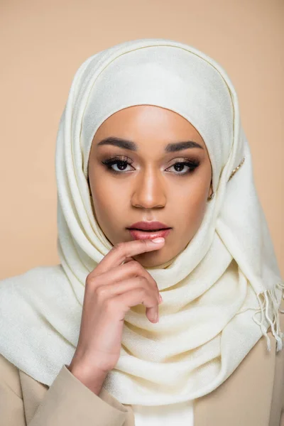 Portrait of young muslim woman in hijab touching lip isolated on beige — Stock Photo