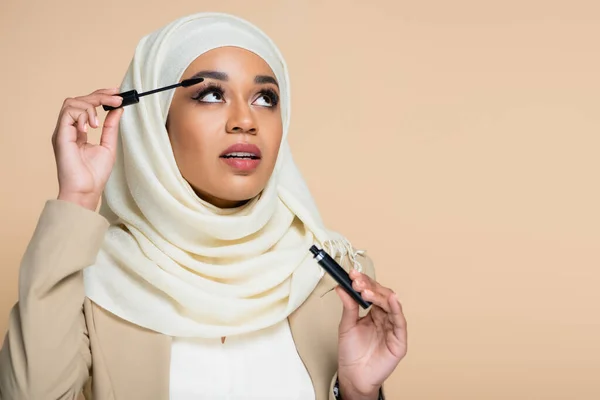Mulher muito muçulmana no hijab aplicando rímel com escova isolada no bege — Fotografia de Stock