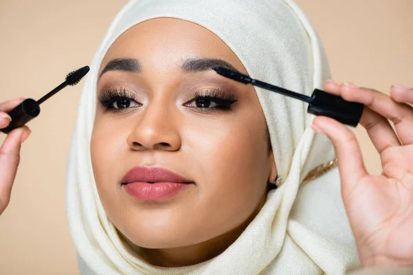 Close up of muslim woman in hijab applying mascara with brushes isolated on beige — Stock Photo