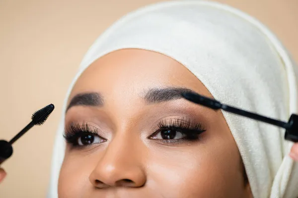 Cropped view of muslim woman in hijab applying mascara with brushes isolated on beige — Stock Photo