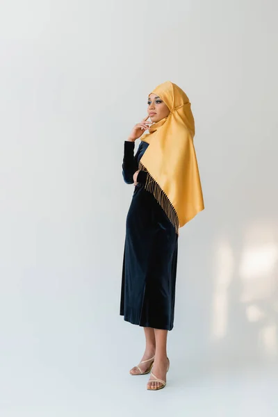 На всю длину мечтательной мусульманки в хиджабе и бархатно-синем платье на белом — стоковое фото