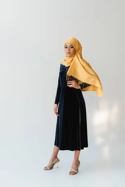 Comprimento total de mulher muçulmana sonhadora em hijab e veludo vestido azul posando com a mão no quadril no branco — Fotografia de Stock