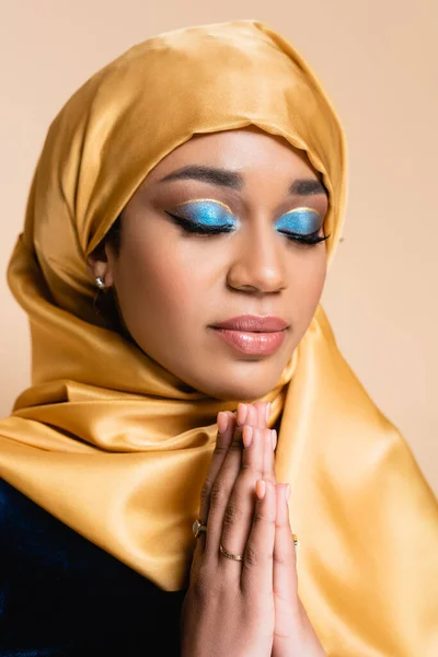 Jovem mulher muçulmana em hijab amarelo com as mãos de oração isolado no bege — Fotografia de Stock