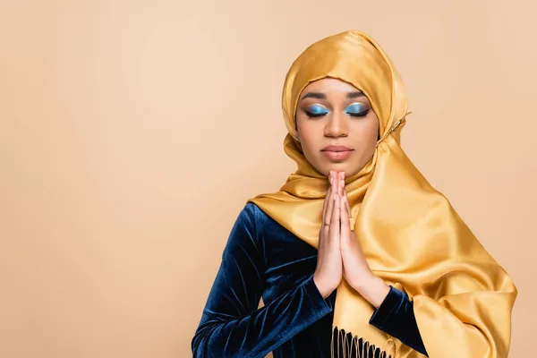 Young muslim woman in hijab standing with praying hands isolated on beige — Stock Photo