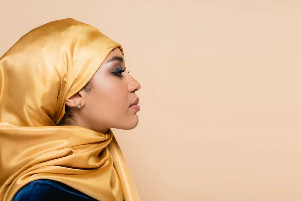 Профиль мусульманки в желтом хиджабе с ярким макияжем, изолированным на бежевом — стоковое фото