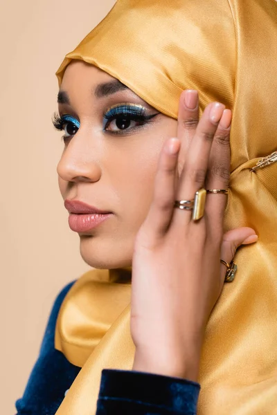 Гарна мусульманка в жовтому хіджабі з золотими кільцями на пальцях позує ізольовано на бежевому — стокове фото