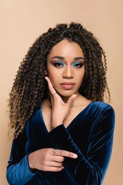 Curly african american woman with bright makeup looking at camera isolated on beige — Stock Photo