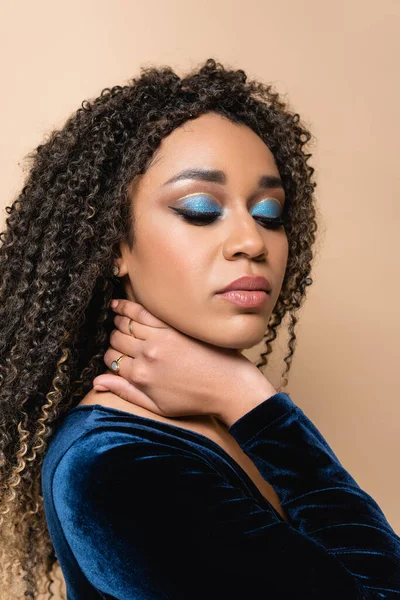 Rizado africano americano mujer con brillante maquillaje posando aislado en beige - foto de stock