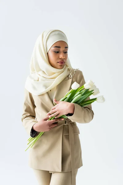 Pretty muslim woman in hijab looking at tulips isolated on white — Stock Photo