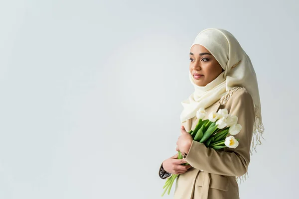 Hübsche muslimische Frau im weißen Hijab hält Tulpen isoliert auf grau — Stockfoto