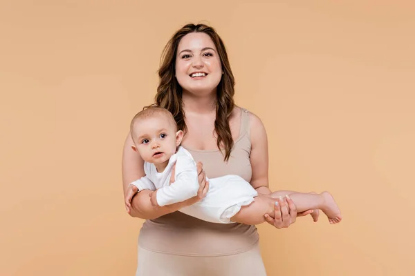 Cheerful plus size woman holding baby daughter isolated on beige — Stock Photo