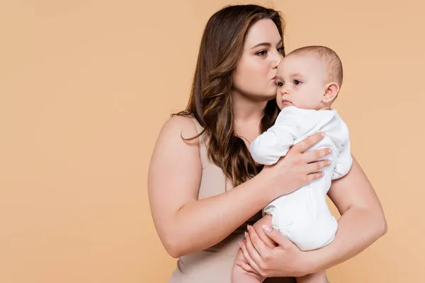 Plus tamaño madre besos bebé hija aislado en beige - foto de stock