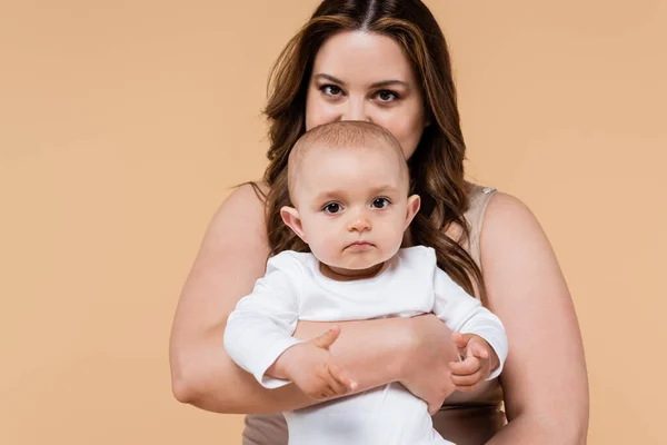 Jeune femme avec surpoids tenant enfant isolé sur beige — Photo de stock