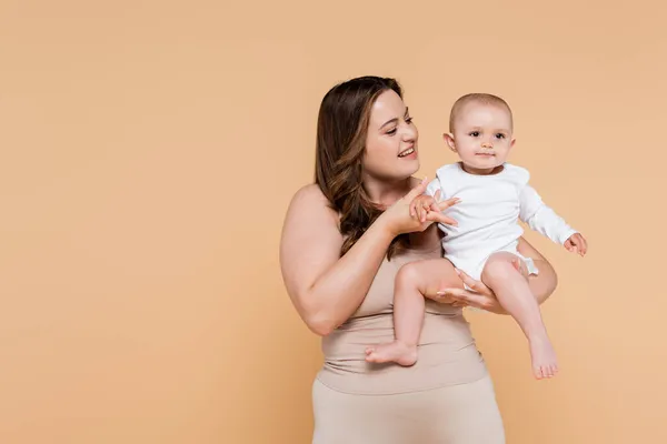 Feliz mujer de talla grande cogida de la mano de niño aislado en beige - foto de stock