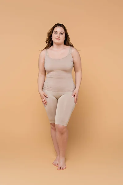 Comprimento total da mulher descalça plus size olhando para a câmera no fundo bege — Fotografia de Stock