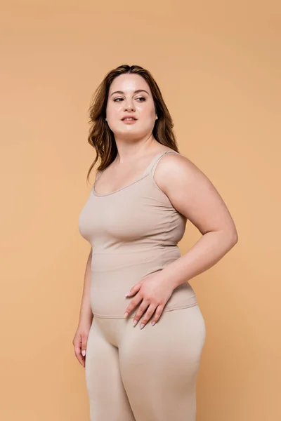 Mujer bonita con sobrepeso mirando hacia otro lado aislado en beige - foto de stock