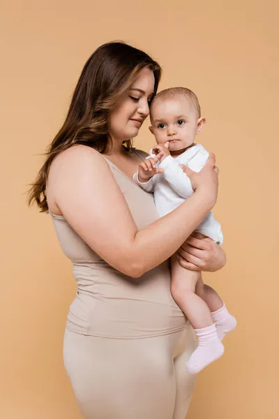 Joven más tamaño mujer abrazando hija aislado en beige - foto de stock