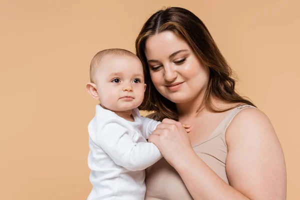 Mulher sorridente com sobrepeso segurando bebê filha isolada no bege — Fotografia de Stock