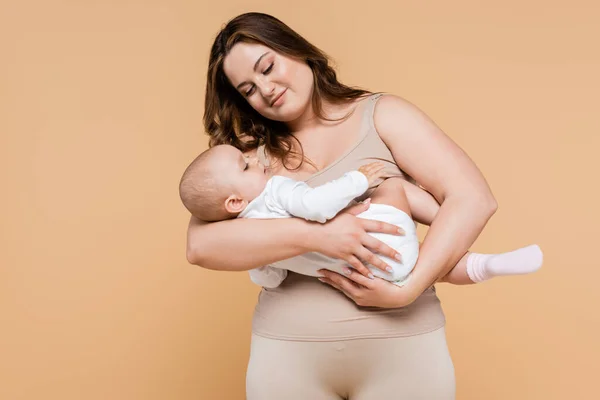 Body positive woman looking at baby daughter isolated on beige — Stock Photo