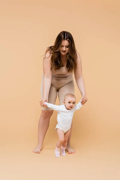 Grande taille femme marchant près de bébé fille sur fond beige — Photo de stock