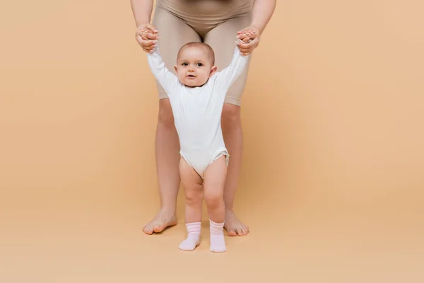 Body positive mother walking near baby daughter on beige background — Stock Photo