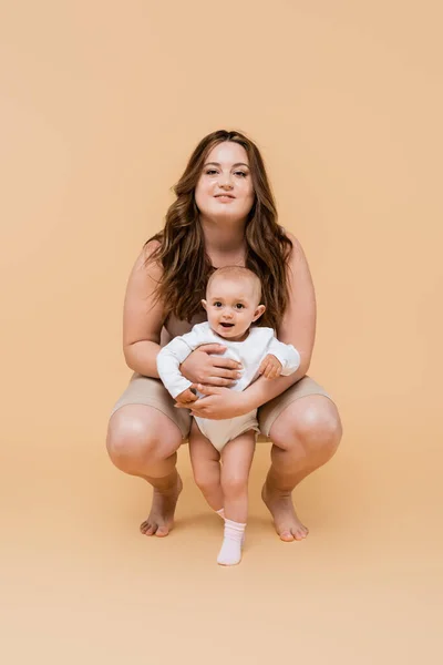Felice plus size mamma abbracciando figlia bambino su sfondo beige — Foto stock