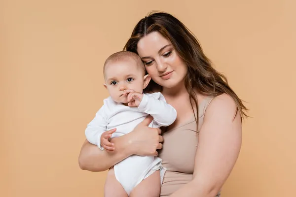 Jovem mãe com sobrepeso segurando bebê isolado no bege — Fotografia de Stock