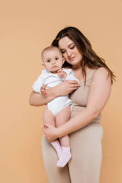 Plus tamaño mujer sosteniendo bebé hija aislado en beige - foto de stock