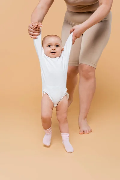 Mujer de talla grande cogida de la mano de la hija del bebé mientras camina sobre fondo beige - foto de stock